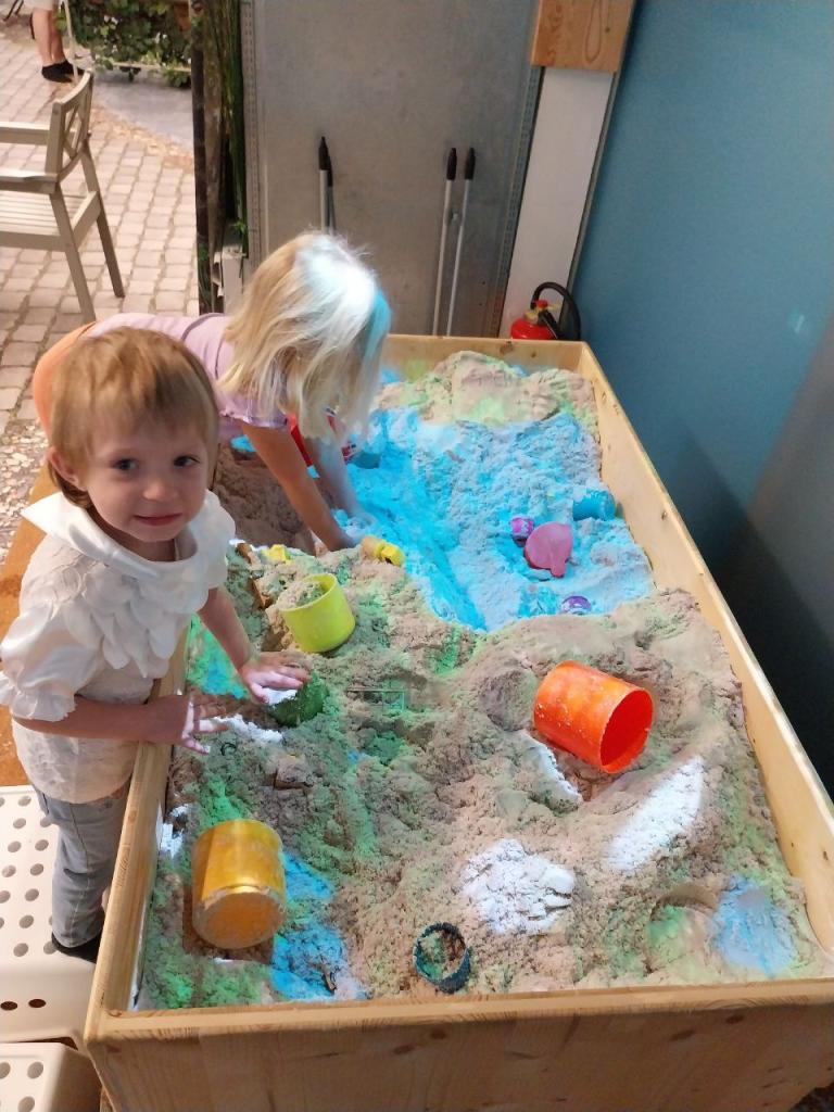 zwei Kleinkinder spielen bei einer Sandkiste und lachen in die Kamera