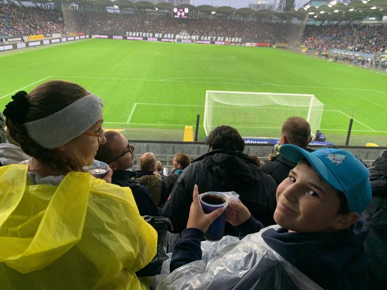 Bub sitzt im Fußballstadion und schaut über die Schulter zurück mit einem Grinsen im Gesicht in die Kamera