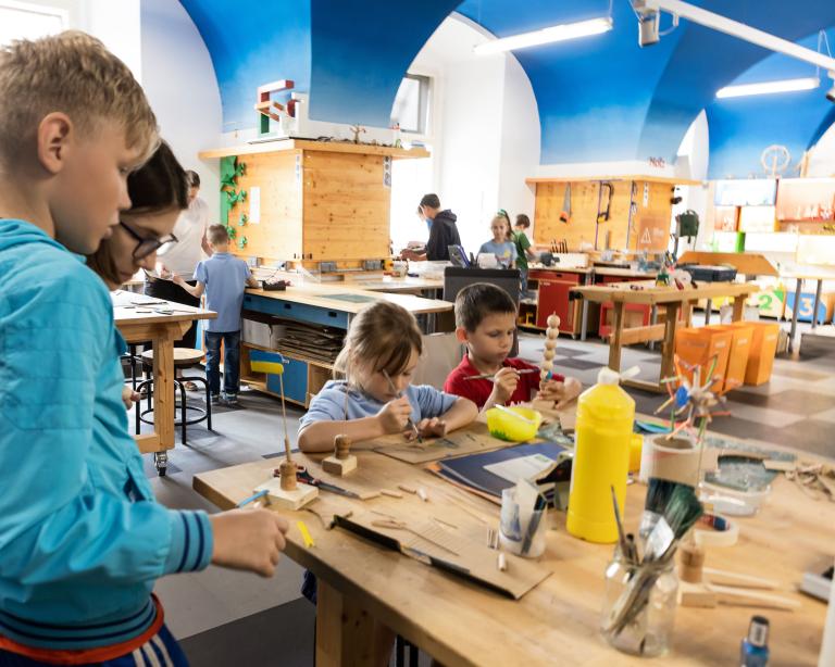 Kinder sitzen in einer Werkstatt und basteln