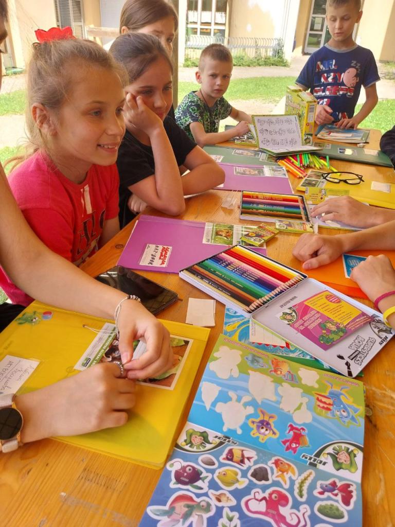 Kinder sitzen draußen an einem Holztisch, sie basteln und malen