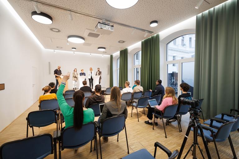 Im großen Eventsaal der Blumenfabrik findet eine Pressekonferenz statt. Das Publikum wird von hinten angeschnitten.