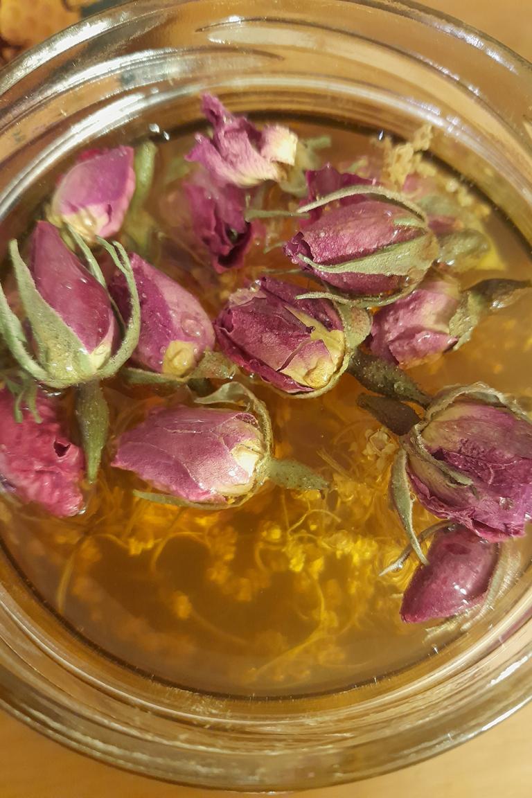 Ein Glas aus der Vogelpersektive. Darin befindet sich Oxymel mit grtrockneten Rosenblüten und Hollunder. 