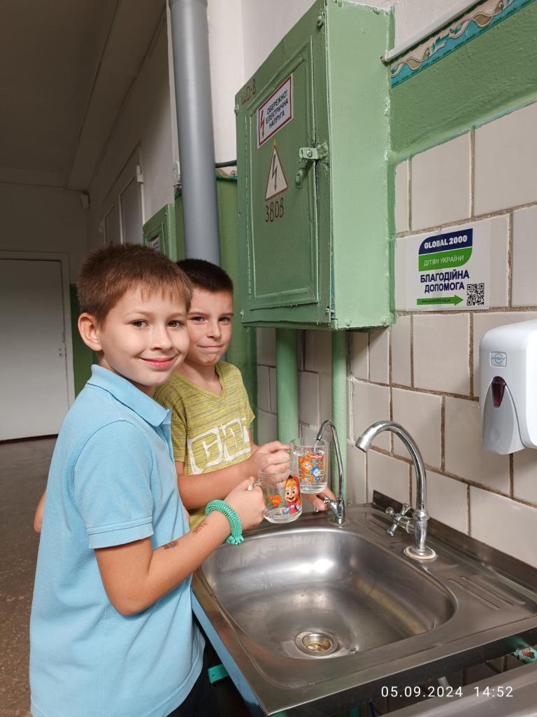 Zwei Buben stehen bei einem Waschbecken und füllen ihre Wassergläser auf