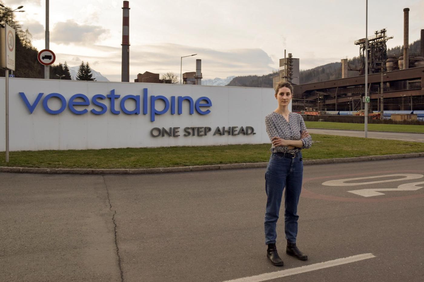 Anna Leitner steht auf der Straße vor dem Schild der Voestalpine