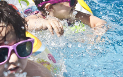 zwei Kinder schwimmen mit Schwimmreifen und Sonnenbrillen