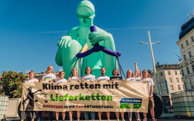 Aktivist:innen halten einen Banner in der Hand mit der Aufschrift "Klimaretten mit Lieferketten". Sie stehen vor einer 10 Meter großen Statue, die Justitia darstellt.