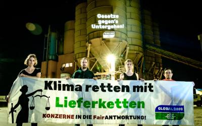 Aktivist:innen stehen vor der Firma Holcim und halten ein großes Banner in die Kamera. Darauf steht "Klima retten mit Lieferketten"