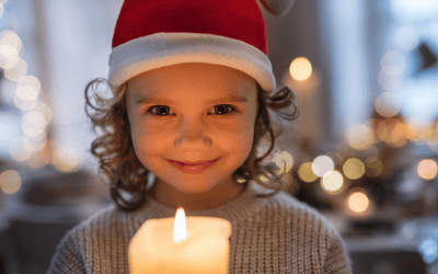 Mädchen mit Weihnachtsmütze schaut in die Kamera und lacht, vor ihr steht eine Herze, die leuchtet. 