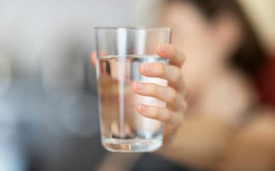 Person (unscharf im Hintergrund) hält Wasserglas