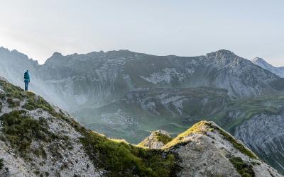 Person in Outdoorkleidung steht auf Berg und schaut in die Ferne