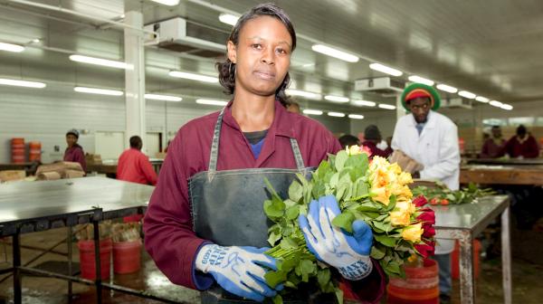 Arbeiterin hält Strauß mit Rosen in Fabrikshalle in der Hand und schaut in die Kamera