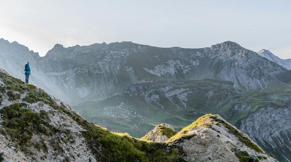 Person in Outdoorkleidung steht auf Berg und schaut in die Ferne